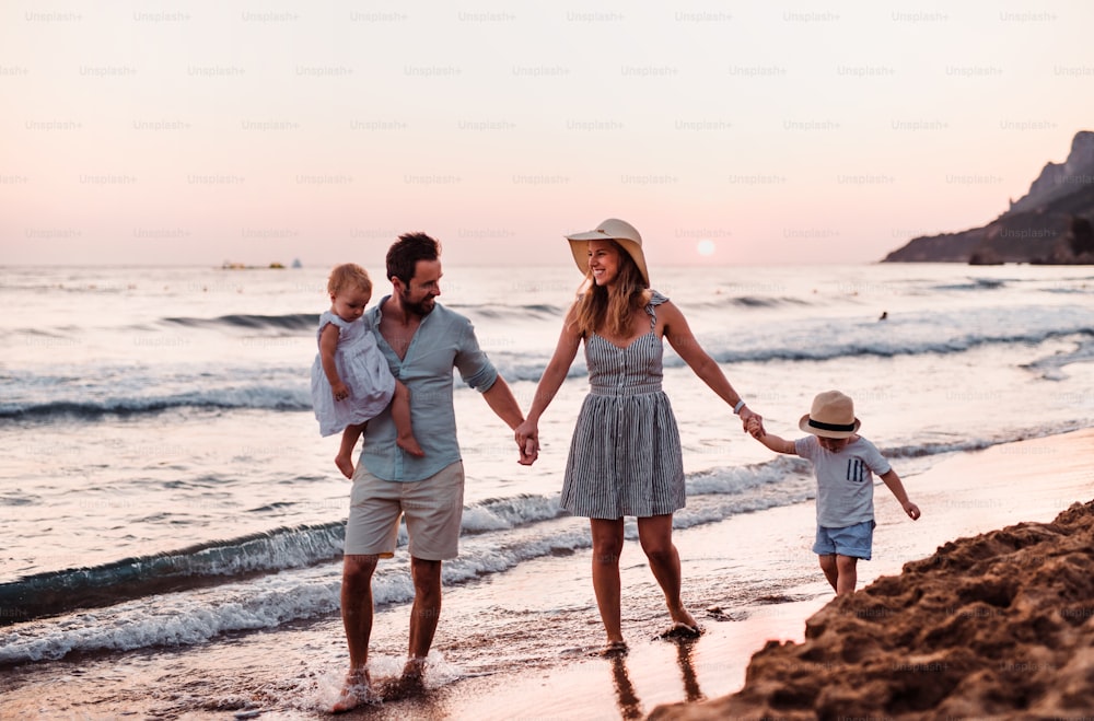 여름 휴가에 해변을 걷고 있는 두 명의 유아 자녀를 둔 젊은 가족.
