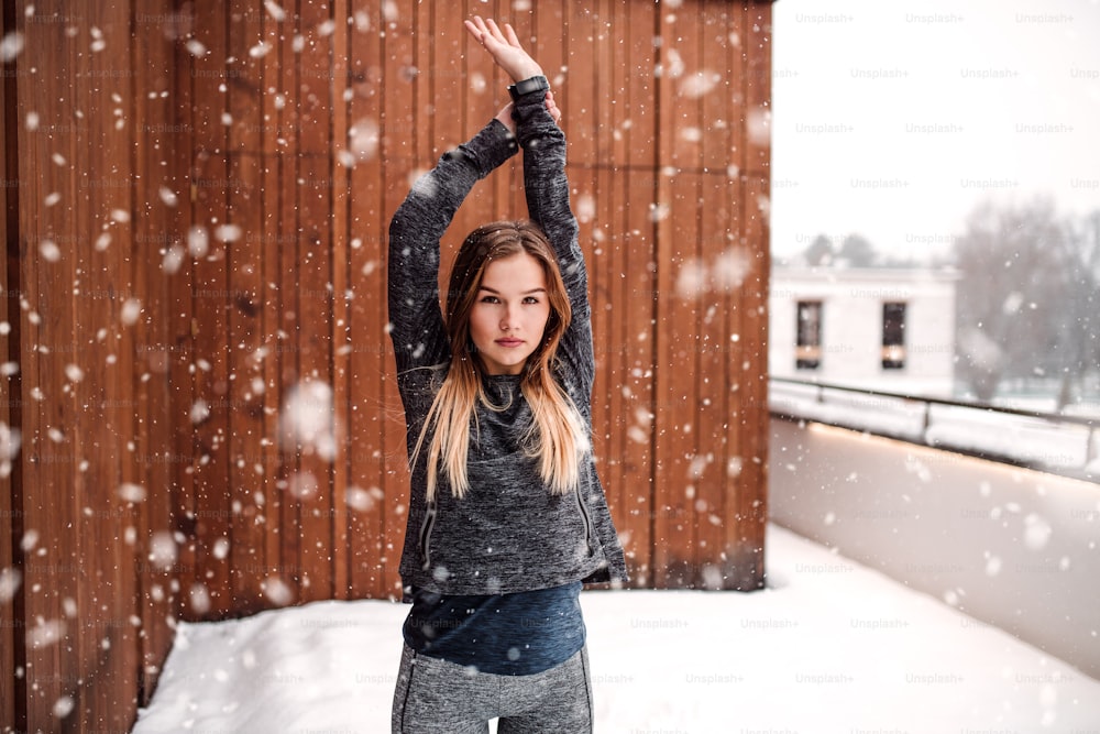 A portrait of young girl or woman doing stretching outdoors on a terrace in winter. Copy space.