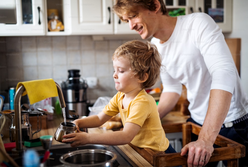 Um jovem pai com um filho pequeno passando o tempo em uma cozinha em casa.