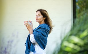 Side view of mature woman with cup of tea resting outdoors in backyard.