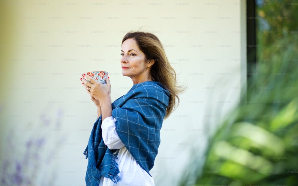 裏庭で屋外で休んでいるお茶を飲む成熟した女性の側面図。