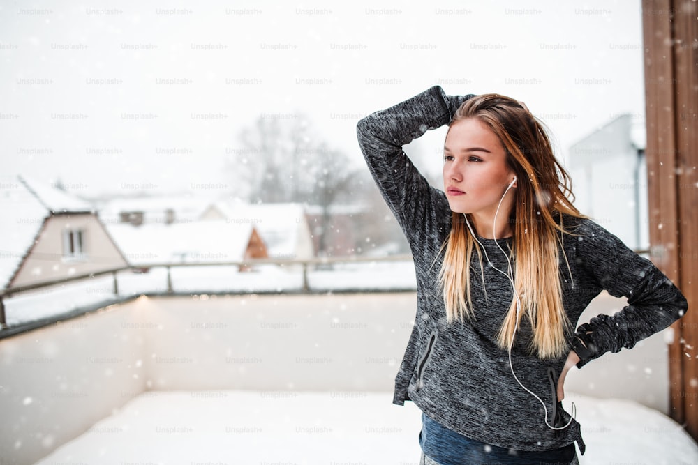 Ein Porträt eines jungen Mädchens oder einer Frau mit Kopfhörern, die sich im Winter draußen auf einer Terrasse dehnen. Speicherplatz kopieren.