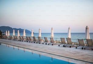 Cadeiras de praia e guarda-sóis em fila na praia tropical, conceito de férias de verão.