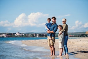 Young family with two small children standing barefoot outdoors on beach.