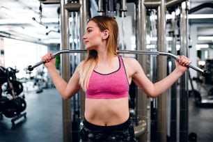 Una vista frontal de una hermosa joven o mujer haciendo entrenamiento de fuerza en un gimnasio.