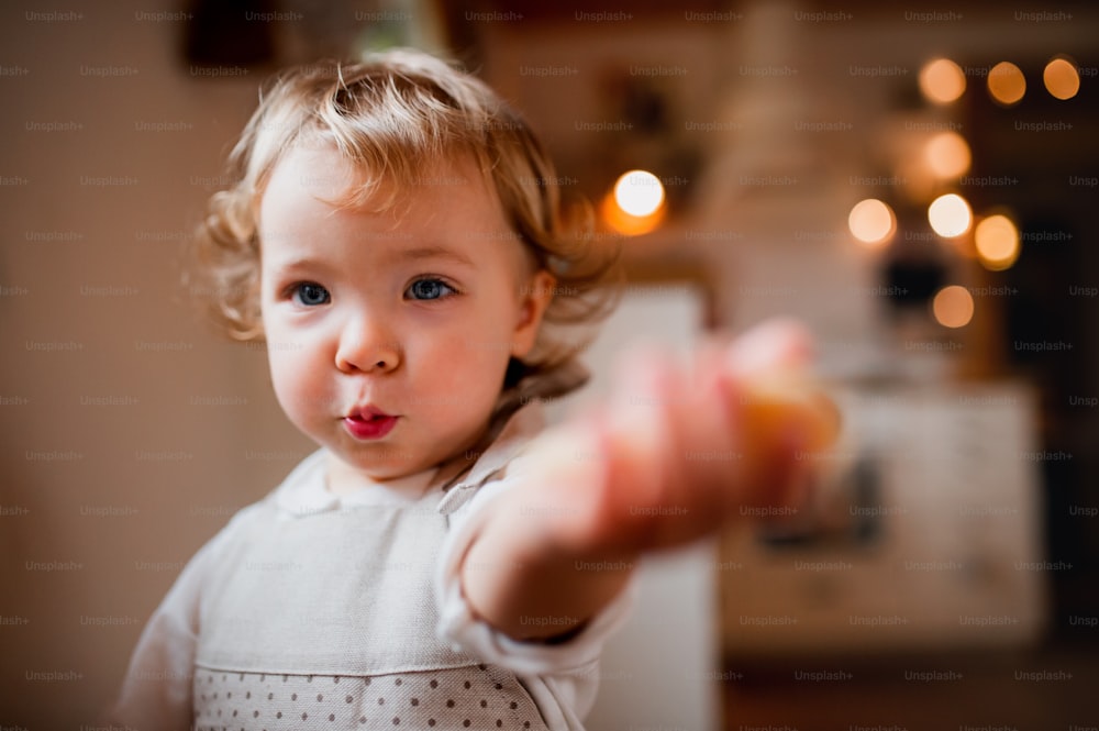 A happy small toddler girl sitting at the table, eating cakes at home.