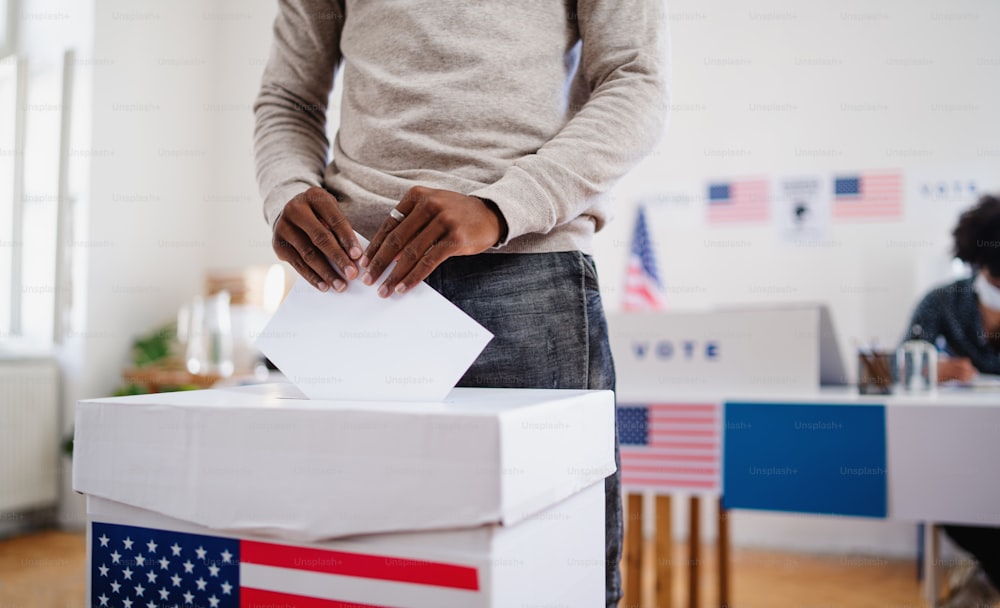 見分けがつかないアフリカ系アメリカ人の男性が投票箱に票を入れる、アメリカの選挙とコロナウイルスのコンセプト。