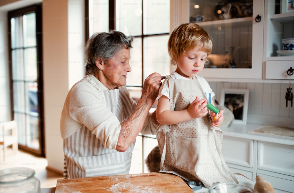 Happy senior great grandmother with small toddler boy making cakes at home.