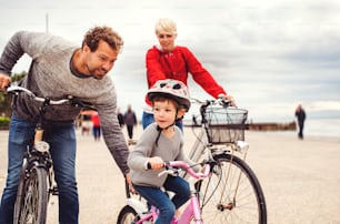 A young family and small daughter with bicycles outdoors on beach.