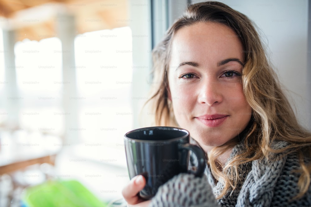 Vista frontal de una mujer joven relajándose en el interior de su casa con una taza de café o té.