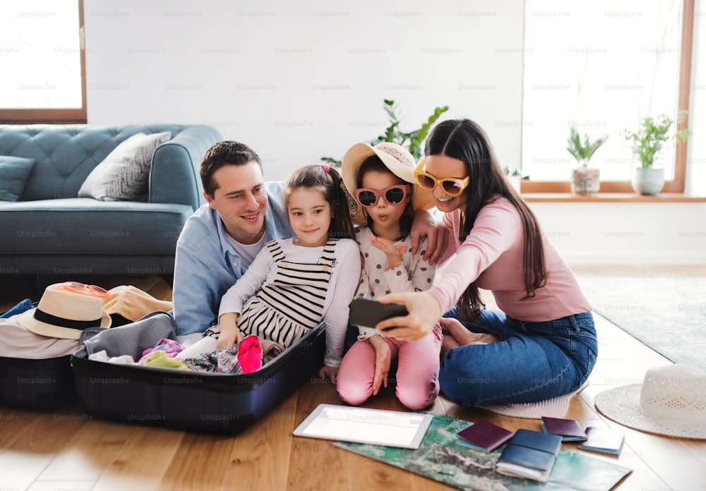 Parents with small daughters indoors at home, taking selfie when packing for summer holiday.