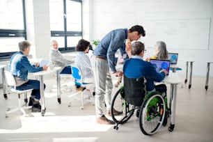 Senior man in wheelchair with teacher attending computer and technology education class.