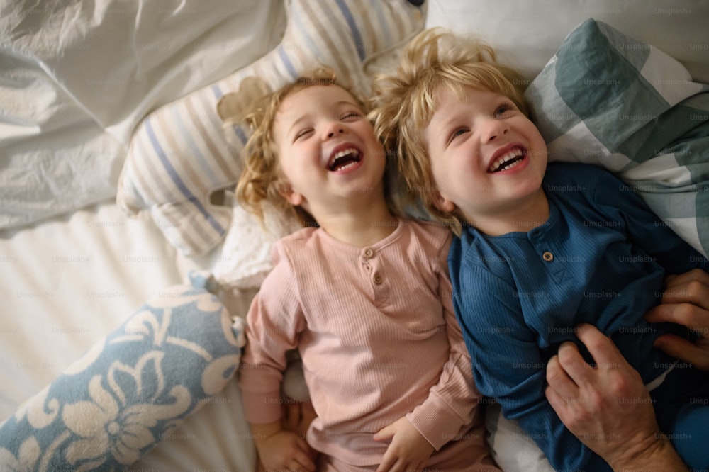 Duas crianças alegres rindo com pai irreconhecível em casa, se divertindo.