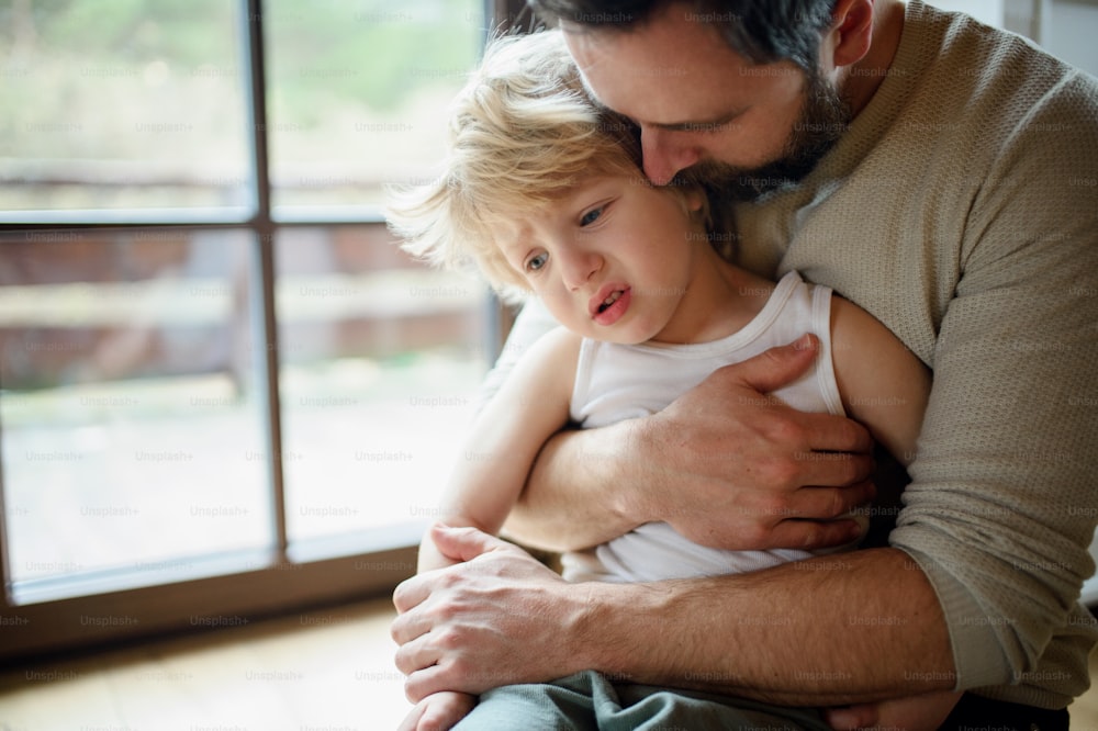 小さな病気の不幸な息子を家の屋内に置き、抱きしめて慰める父親。