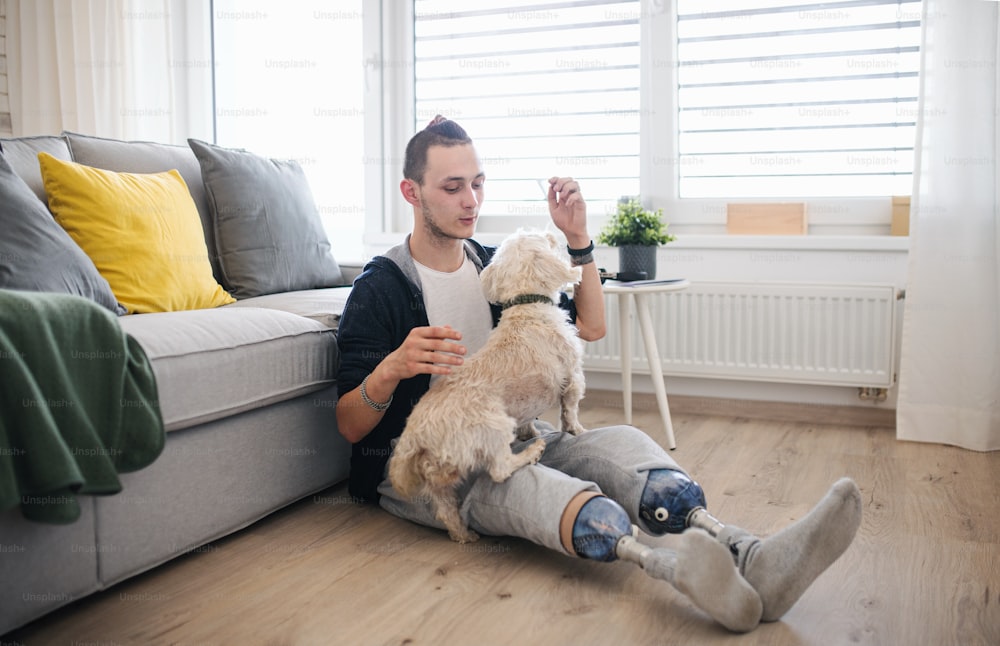 Ein Porträt eines behinderten jungen Mannes, der zu Hause mit Hund spielt, Beinprothesenkonzept.