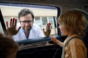 Doctor coming to see and greet family in isolation, car window glass separating them.