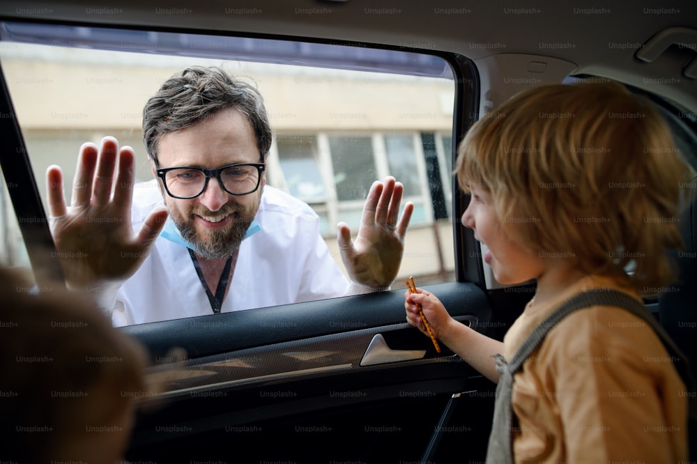 Arzt kommt, um Familie in Isolation zu sehen und zu begrüßen, Autofensterglas trennt sie.