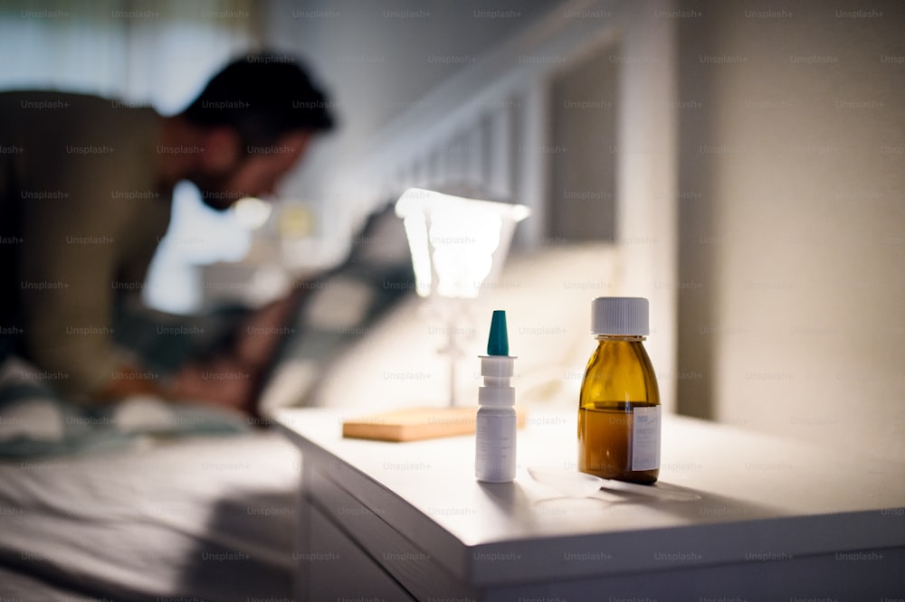 Flacone di sciroppo di farmaci e spray nasale sul tavolo da comodino a casa, concetto di medicina e malattia.