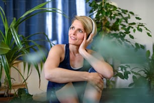 Front view of happy young woman with headphones indoors at home, resting.