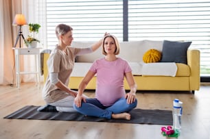 Contented pregnant woman doing yoga exercise with instructor at home.