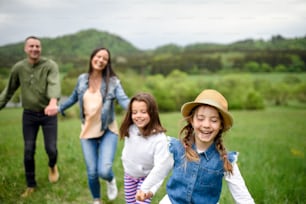 Happy family with two small daughters running outdoors in spring nature, holding hands.