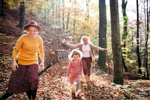 Small girl with mother and grandmother on a walk in autumn forest, having fun.