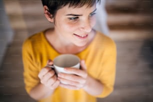 自宅でコーヒーを飲む若い女性の正面図。ガラス越しに撮影。