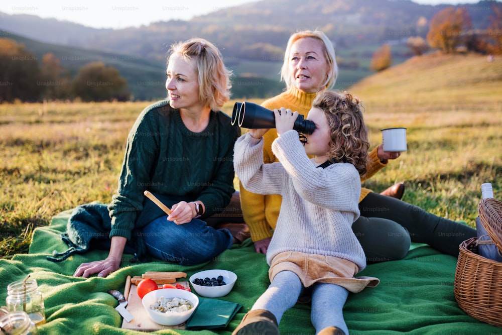 Niña feliz con la madre y la abuela haciendo un picnic en la naturaleza, usando binoculares.