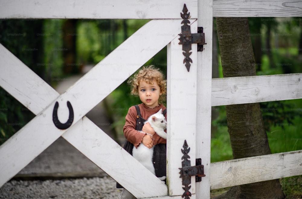 Porträt eines kleinen Mädchens mit Katze, das auf dem Bauernhof steht und in die Kamera schaut.