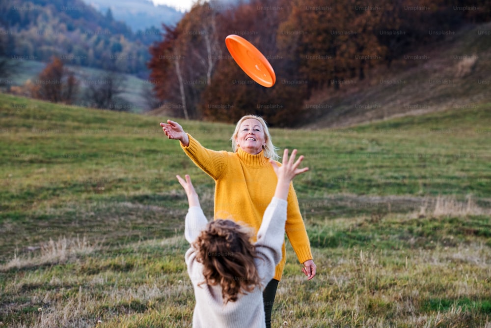 Small girl with grandmother on a walk in autumn nature, playing with flying disc.