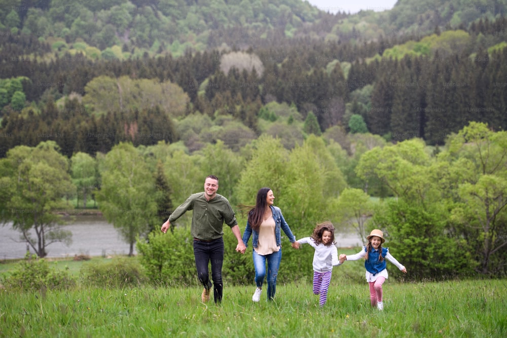 Happy family with two small daughters running outdoors in spring nature, holding hands.