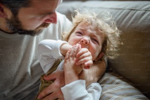 Père mature avec une petite fille malade pleurant en bas âge à l’intérieur à la maison.