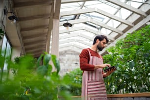 温室に立って作業しているタブレットを持つ男性の庭師の低角度ビュー。