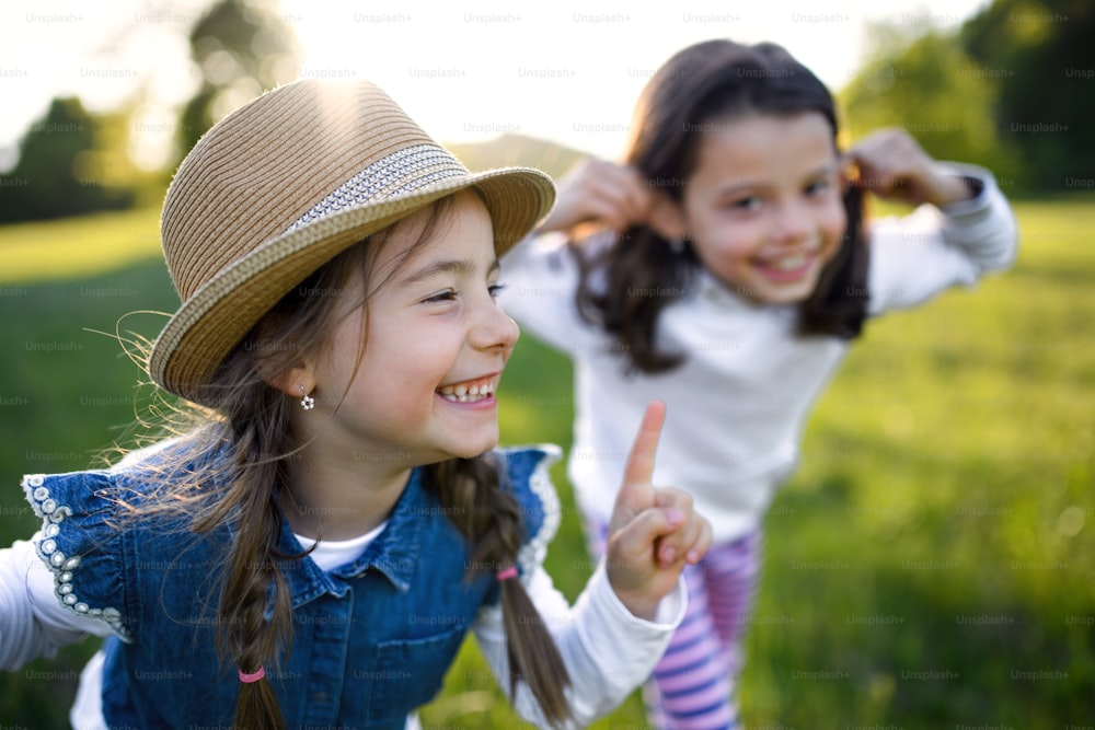 Vorderansicht Porträt von zwei kleinen Mädchen, die draußen in der Frühlingsnatur stehen und lachen.