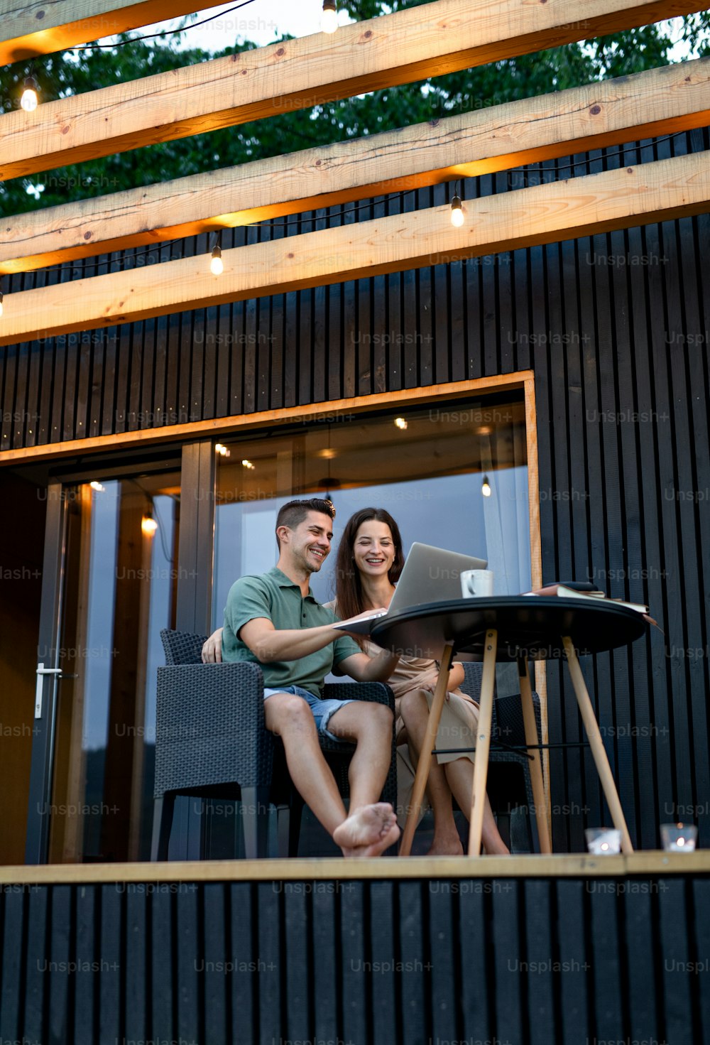 Giovane coppia con laptop seduta all'aperto, fine settimana in una casa container in campagna.