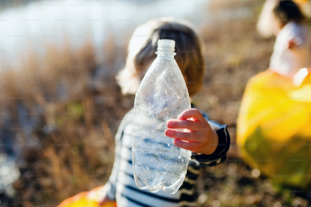 Unrecognizable small child with plastic bottle collecting rubbish outdoors in nature, plogging concept.