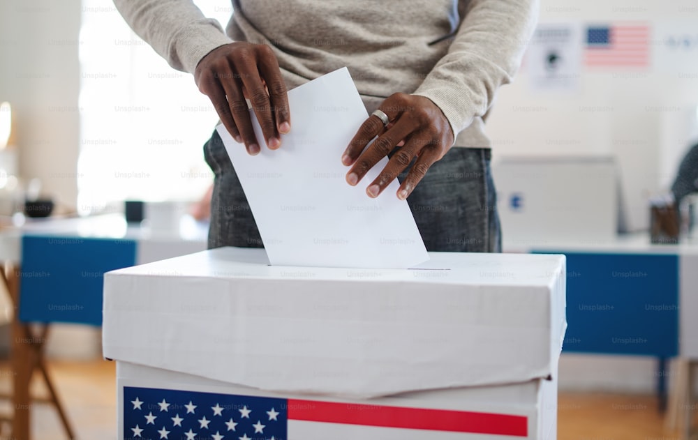 Homem afro-americano irreconhecível colocando seu voto nas urnas, eleições nos EUA e conceito de coronavírus.