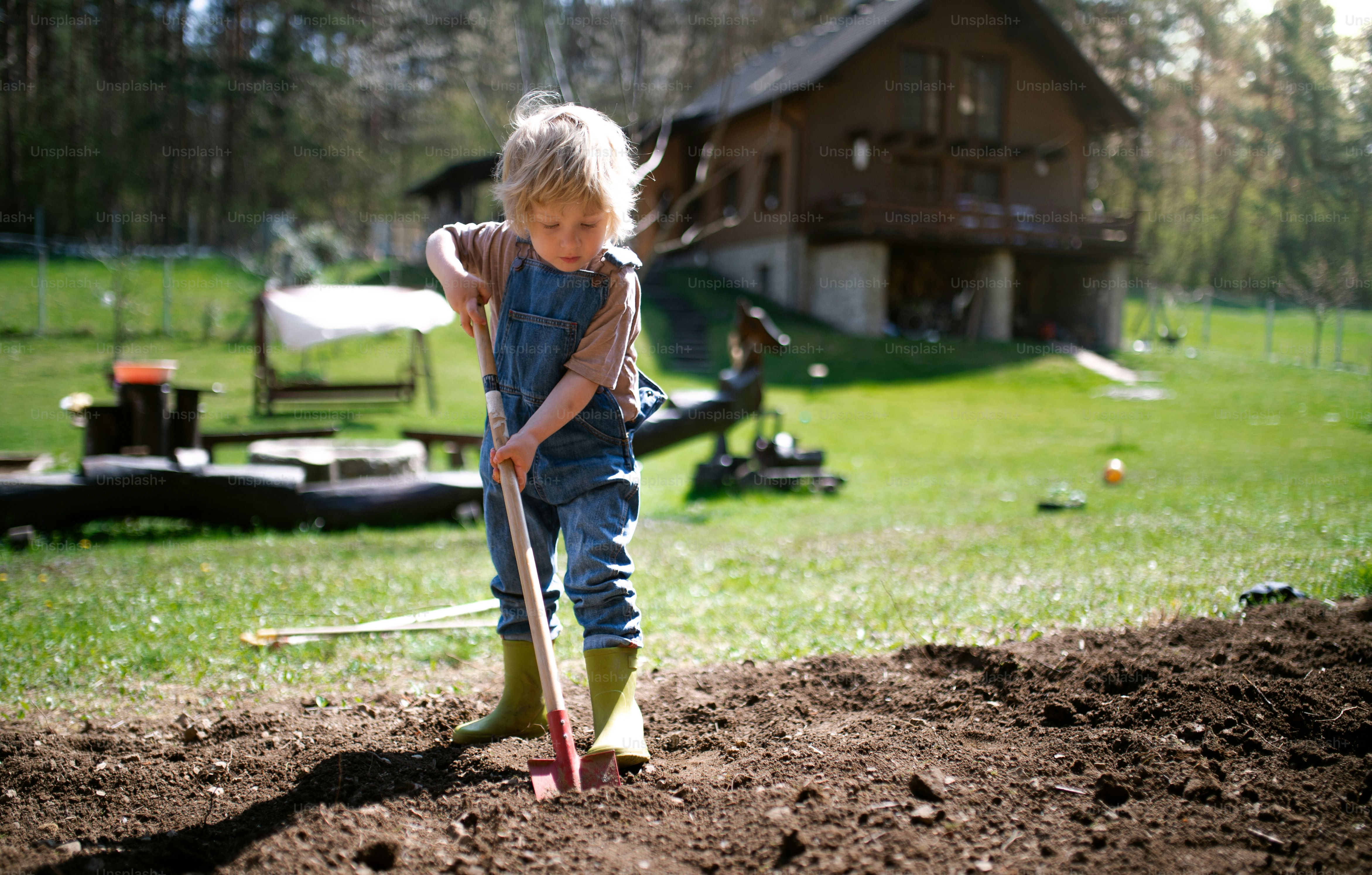 Niño pequeño feliz que trabaja al aire libre en el jardín, concepto de estilo de vida sostenible