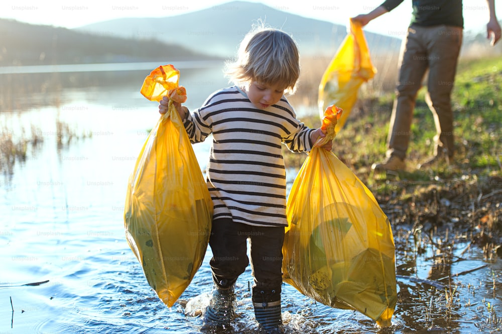 Padre irriconoscibile con figlio piccolo che raccoglie rifiuti all'aperto nella natura, concetto di plogging.