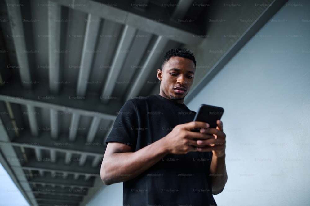 Low angle view of young black man outdoors in city, using smartphone.