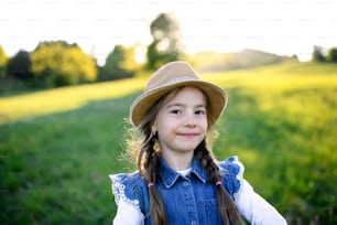Front view portrait of small girl standing outdoors in spring nature, looking at camera.