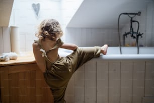 Rear view of small toddler child climbing into bath tub indoors at home.