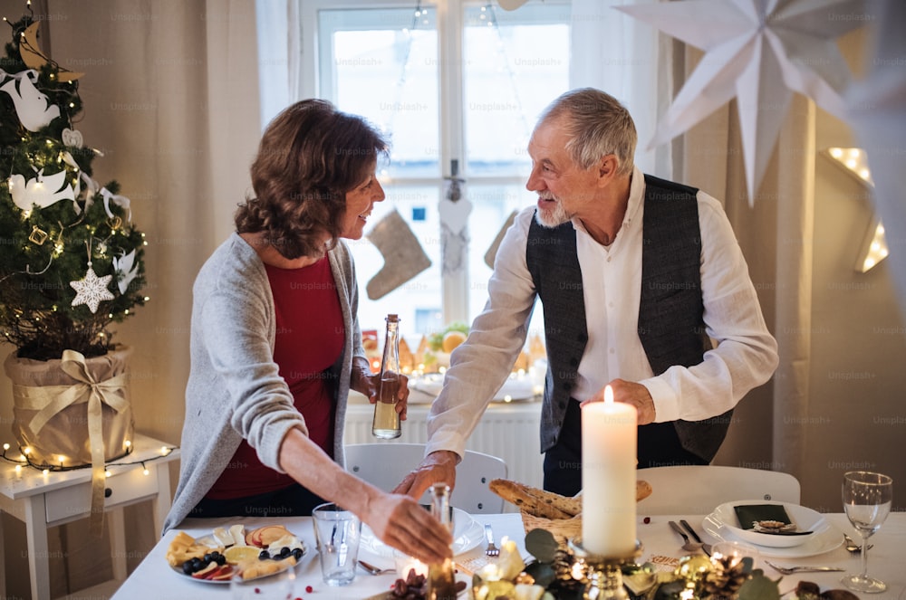 Heureux couple de personnes âgées à l’intérieur à la maison mettant la table au moment de Noël.