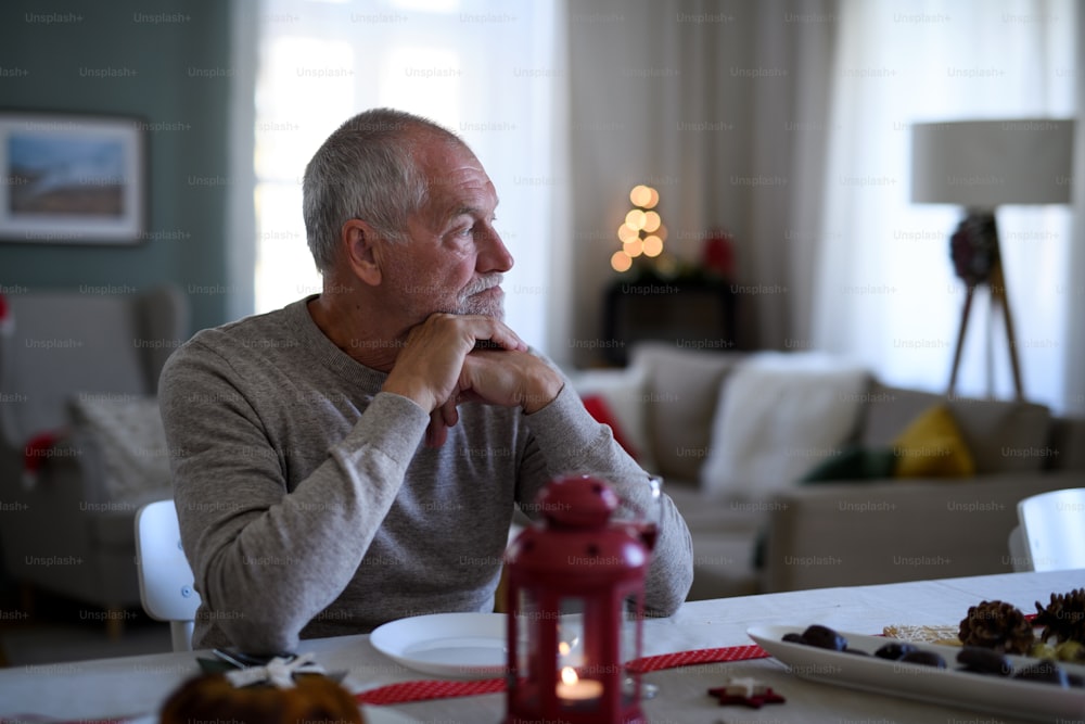 Porträt eines einsamen älteren Mannes, der zu Weihnachten drinnen am Tisch sitzt, Einsamkeitskonzept.