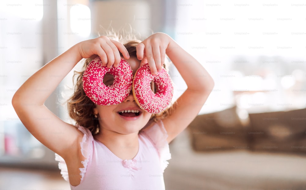 A portrait of small girl with two doughnuts at home, having fun.