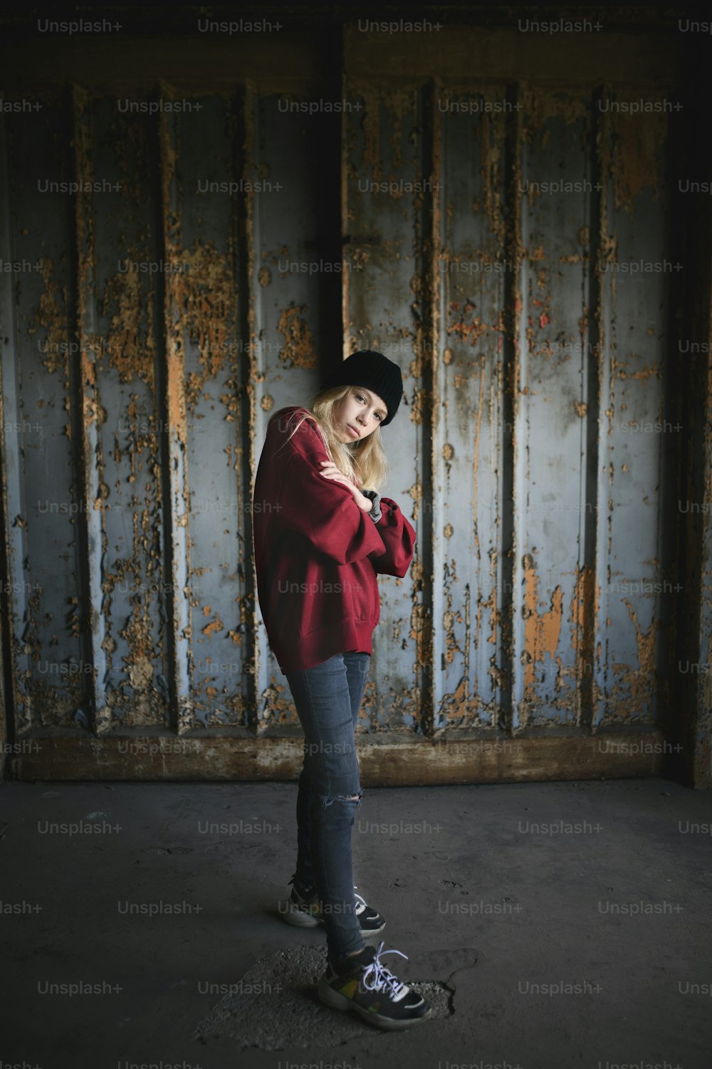 Retrato de vista frontal de una adolescente rubia de pie en el interior de un edificio abandonado.