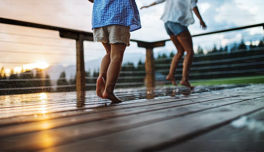 Legs of unrecognizable mother with small daughter playing on patio of wooden cabin, holiday in nature concept.