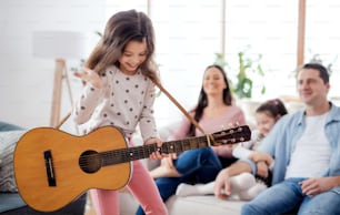 ギターで楽しんでいる、自宅で屋内で家族と小さな女の子の肖像画。