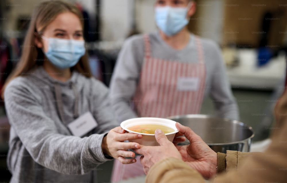 Voluntarios sirviendo sopa caliente para enfermos y personas sin hogar en el centro de donaciones de caridad de la comunidad, el banco de alimentos y el concepto de coronavirus.