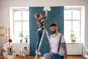 Felice coppia di adulti medi che cambia la lampadina all'interno di casa, trasferimento e concetto fai-da-te.